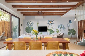 A modern dining area with a wooden table and yellow chairs, a sofa, and a TV mounted on the wall. - "Rana Curiosa" @BlueDeerTulum - 4 Bed+4.5 Bath LUX Villa - Pool, Jacuzzi, Staff (Tulum)