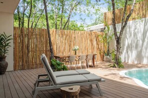 Een houten terras met een lounge stoel, een eettafel met stoelen en een zwembad.