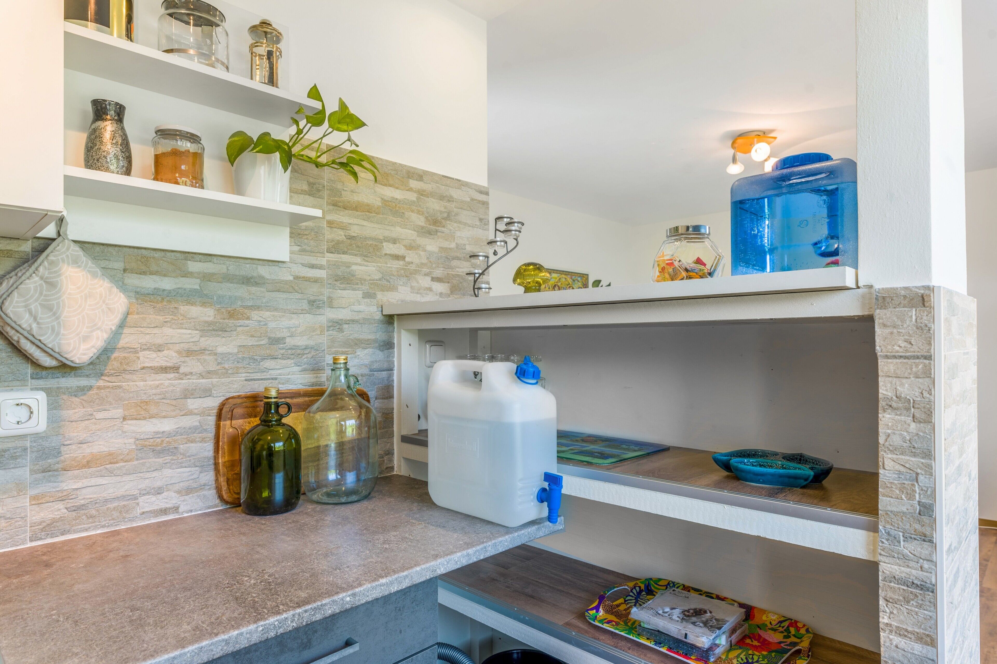A kitchen with a stone backsplash, a sink, and various storage containers on shelves.