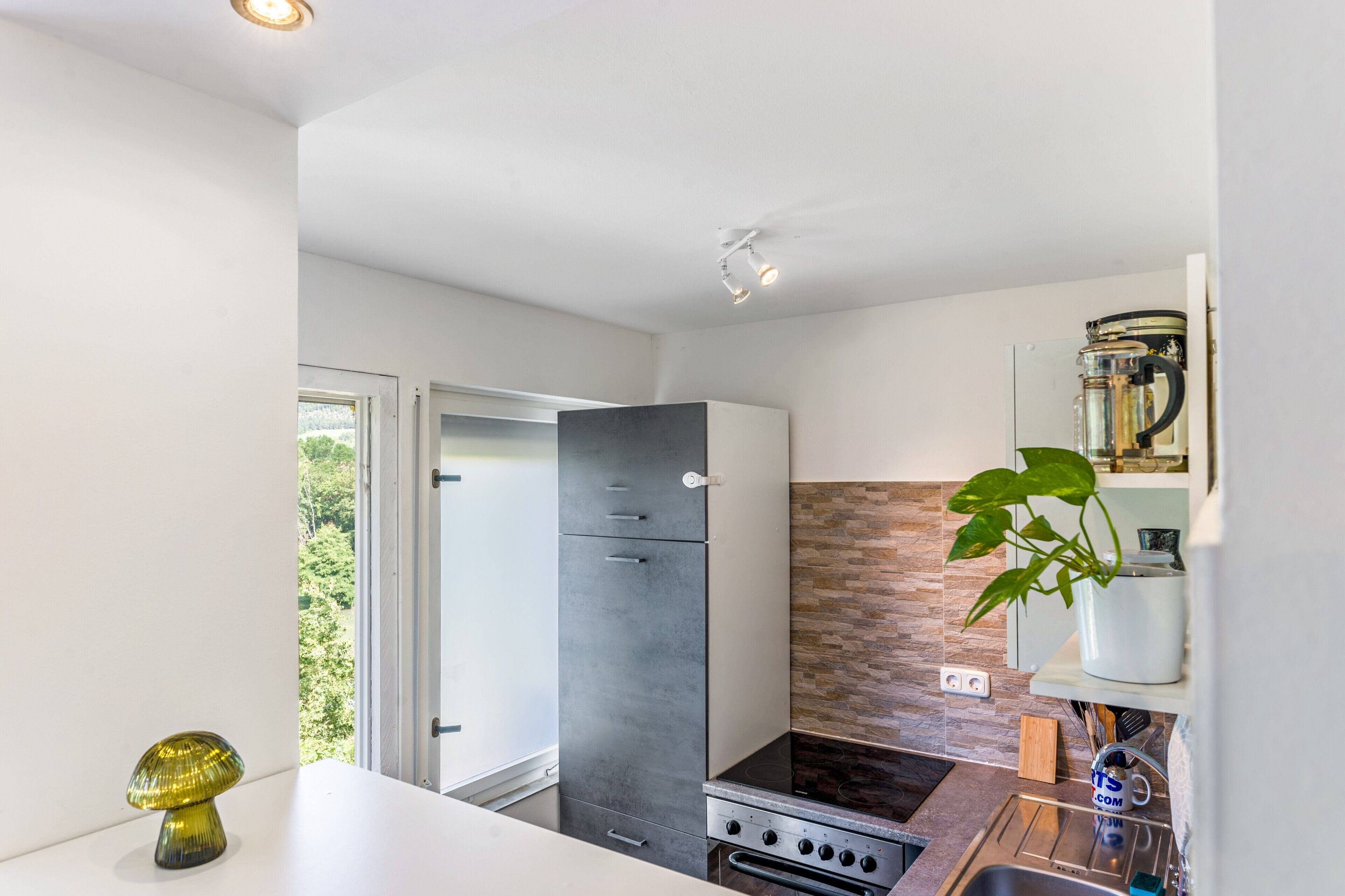 A modern kitchen with a built-in stove, a refrigerator, and a window with a view of greenery.