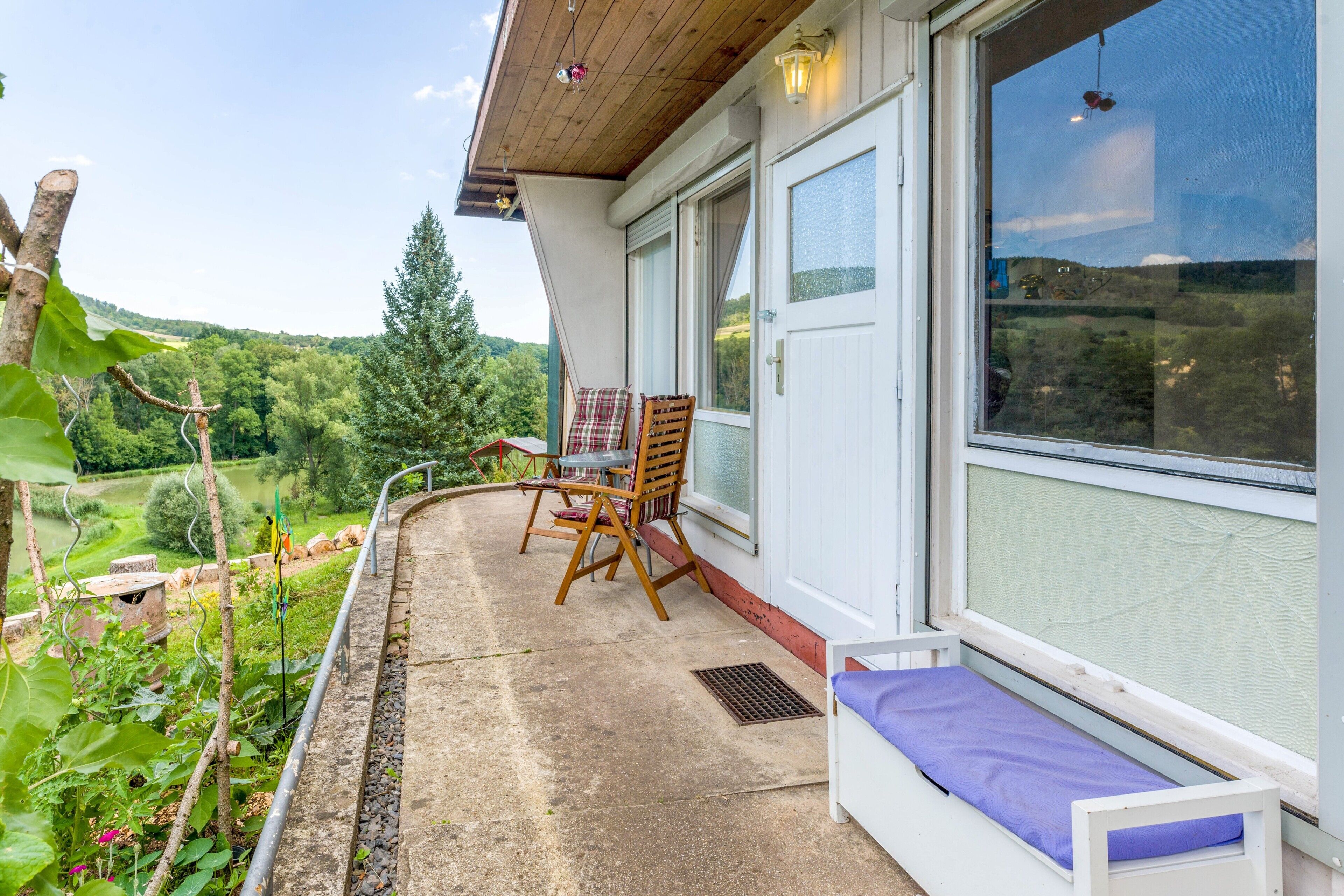 Un balcone con una sedia di legno e un tavolino, affacciato su un paesaggio verdeggiante e rigoglioso.