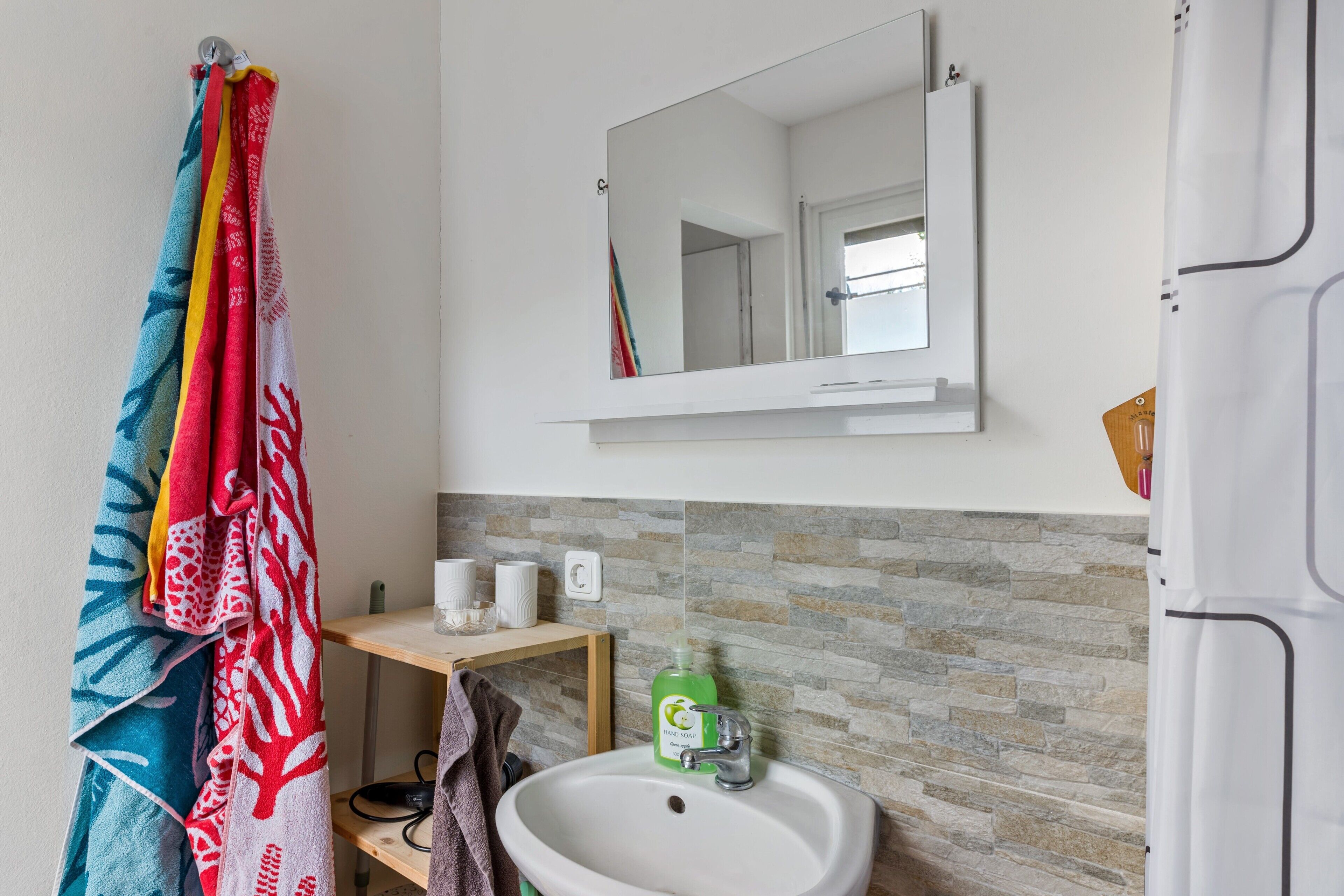 A bathroom with a white sink, a mirror above it, and a towel rack with colorful towels.