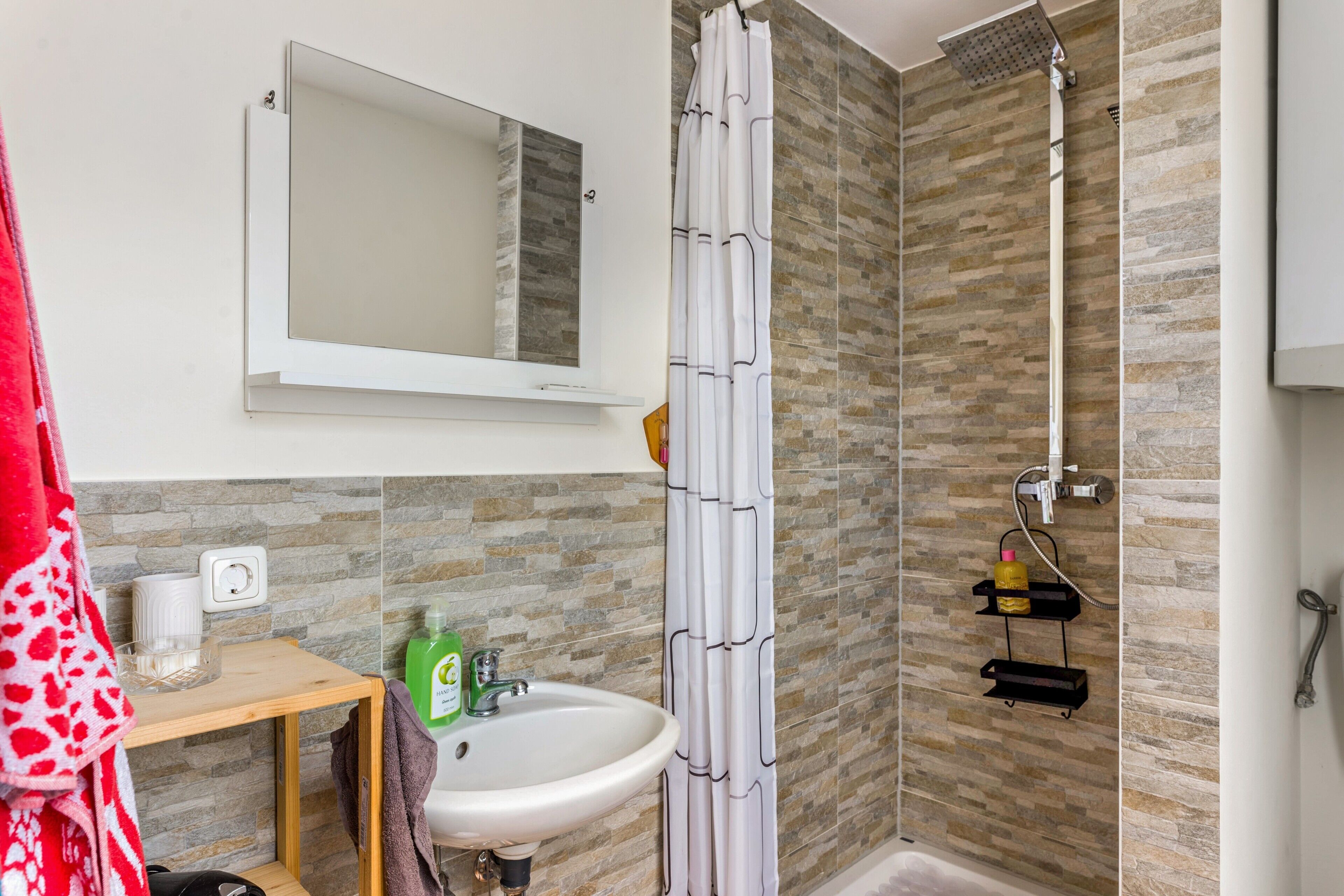 Une salle de bain avec une douche, un lavabo, un miroir et un porte-serviettes.