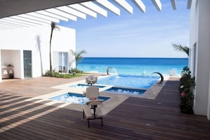 A pool area with a view of the ocean, wooden deck, and a chair. - Beachfront Studio w/ Balcony and Ocean View (Cancún)