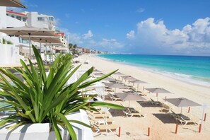 A beach with white umbrellas and lounge chairs, a clear blue sky, and a view of the ocean. - Beachfront studio 2/ Amazing Caribbean view (Cancún)