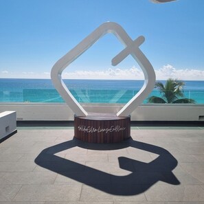 A modern sculpture with a hashtag inscription on a circular base, overlooking a clear blue ocean. - Beachfront studio 2/ Amazing Caribbean view (Cancún)