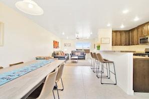 A modern kitchen with a central island, a dining area with a long table, and a living space with a sofa and chairs. - Updated Dog Friendly Condo with Pool & Hot Tub - Close to National Parks (Moab)