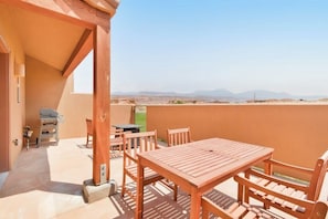 An outdoor patio with a wooden table and chairs, a grill, and a view of distant mountains. - Updated Dog Friendly Condo with Pool & Hot Tub - Close to National Parks (Moab)