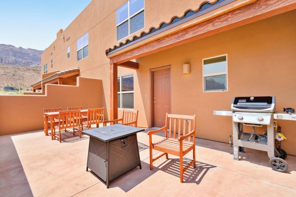 An outdoor patio with a grill, wooden chairs, and a table.
