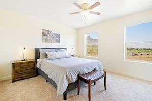 A bedroom with a bed, nightstand, bench, ceiling fan, and large windows. - Updated Dog Friendly Condo with Pool & Hot Tub - Close to National Parks (Moab)