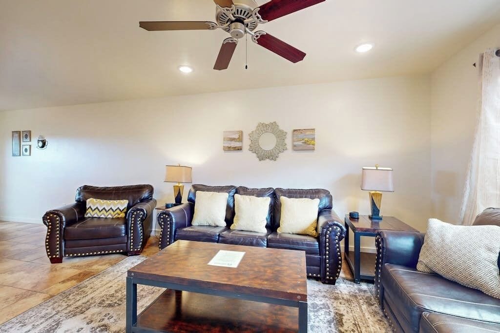A living room with a ceiling fan, a sofa set, a coffee table, and wall-mounted lamps.