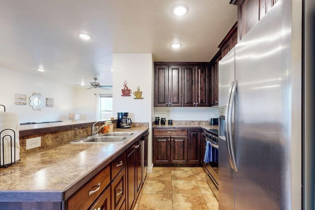 A kitchen with dark wooden cabinets, a stainless steel refrigerator, and a granite countertop.