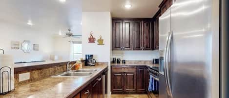 A kitchen with dark wooden cabinets, a stainless steel refrigerator, and a granite countertop.