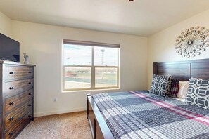 A bedroom with a large window, a bed with patterned bedding, a dresser, and a decorative wall piece. - Spacious Townhouse with Shared Heated Pool, Tennis Courts, & Balcony Views (Moab)