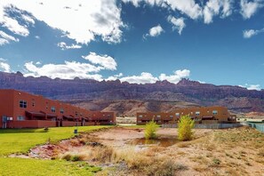 A building complex with multiple red-roofed structures, a grassy area, and a mountainous backdrop. - Spacious Townhouse with Shared Heated Pool, Tennis Courts, & Balcony Views (Moab)