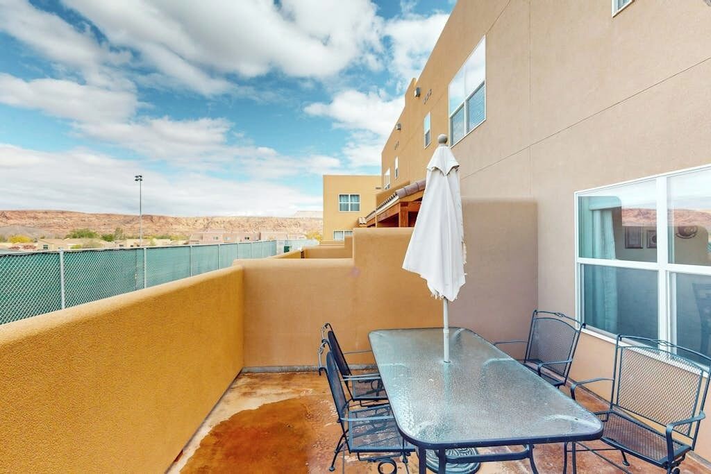 Ein Balkon mit Tisch und Stühlen, einem weißen Sonnenschirm und Blick auf die Wüstenlandschaft.