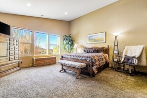 A bedroom with a large bed, a dresser, a bench, a chair, and a television. - Colorful Condo with Shared Pool and Hot Tub - Close to Golf & Arches National Park (Moab)