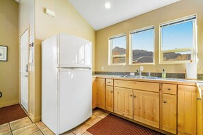 Una cocina con armarios de madera, un refrigerador blanco, un lavamanos y ventanas con vistas.