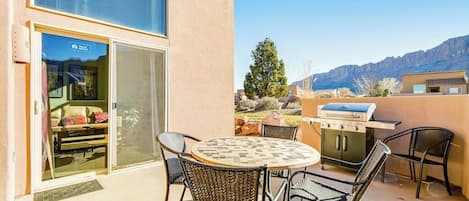 Een terras met een ronde tafel en stoelen, een barbecue en een schuifdeur naar een kamer.
