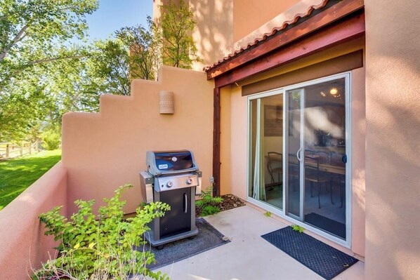 A patio area with a barbecue grill, a sliding glass door, and a small outdoor seating area. - Dog-Friendly Condo on Golf Course with Free WiFi & Seasonal Pool (Moab)