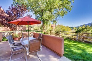 Eine Terrasse im Freien mit Tisch und Stühlen, einem roten Sonnenschirm und einer gepolsterten Bank.