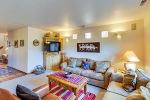 A living room with a sofa, a coffee table, a television, and wall-mounted lighting. - Dog-Friendly Condo on Golf Course with Free WiFi & Seasonal Pool (Moab)