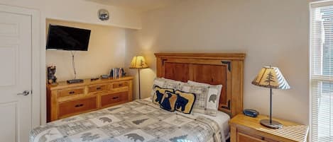 Un dormitorio con una cama, un televisor montado en la pared, un aparador de madera y dos lámparas de noche.