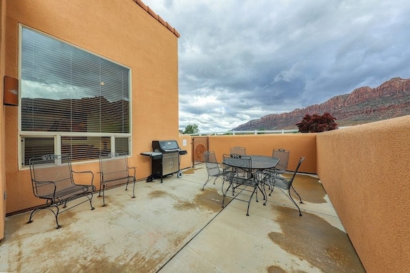 An outdoor patio with a grill, seating, and a view of a mountain range. - Spacious Moab Townhouse with Seasonal Pool and Hot Tub - Views and Hiking Nearby (Moab)