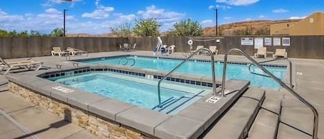 A pool area with two pools, lounge chairs, and a stone wall.