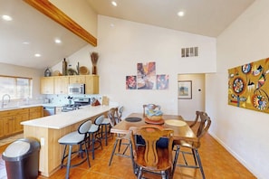 A modern kitchen with a central island, dining area with chairs, and artwork on the walls. - Spacious Moab Townhouse with Seasonal Pool and Hot Tub - Views and Hiking Nearby (Moab)