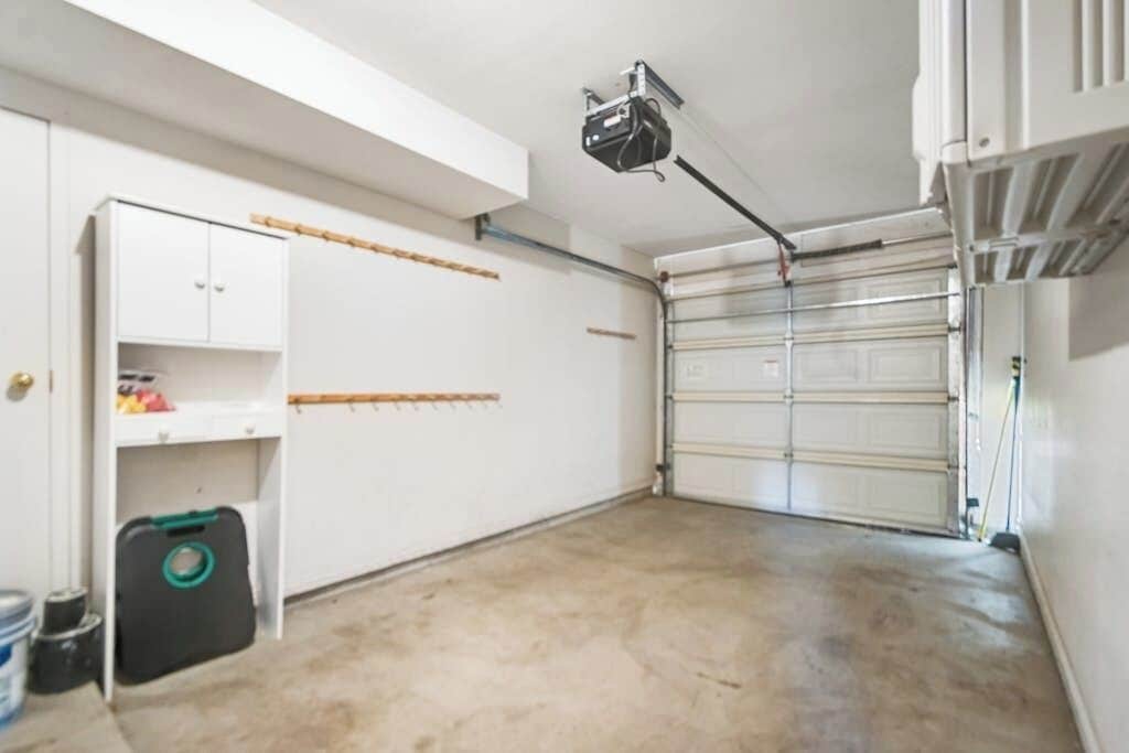 A garage with a white door, a ceiling-mounted projector, and a white cabinet with shelves.