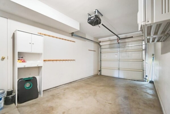 A garage with a white door, a ceiling-mounted projector, and a white cabinet with shelves. - Remodeled Townhouse with Pool, Private Hot tub & Fireplace - Near National Park (Moab)