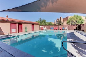 A swimming pool with a shaded area, a red door, and a fenced backyard with lounge chairs. - Condo with Beautiful Red Rock Vistas, Seasonal Pool, Fireplace, Grill, and WiFi (Moab)