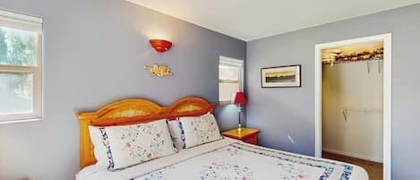A bedroom with a bed, a nightstand, a wall-mounted lamp, a ceiling fan, and a door leading to another room.