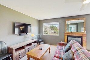 A living room with a television, a fireplace, a sofa, and a window. - Condo with Beautiful Red Rock Vistas, Seasonal Pool, Fireplace, Grill, and WiFi (Moab)