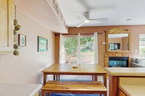 A dining area with a wooden table and bench, a ceiling fan, and a view of the outdoors through a glass door. - Condo with Beautiful Red Rock Vistas, Seasonal Pool, Fireplace, Grill, and WiFi (Moab)