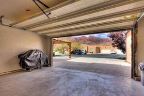 Eine Garage mit einem überdachten Grillwagen, freier Sicht auf parkende Autos und einem Gebäude mit rotem Dach im Hintergrund.