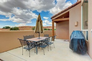 Eine Terrasse im Freien mit Tisch, Stühlen, Sonnenschirm und Grill.