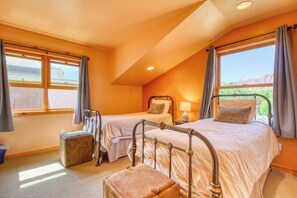 Ein Schlafzimmer mit zwei Betten, einem Fenster mit Vorhängen, einem Nachttisch mit Lampe und einem Koffer auf dem Boden.