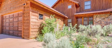 Eine zweistöckige Holzhütte mit Garage, umgeben von einem angelegten Garten mit verschiedenen Sträuchern und Blumen.