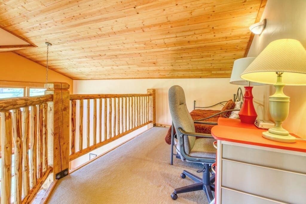 Une pièce avec un plafond en bois, un bureau avec une lampe et une chaise.