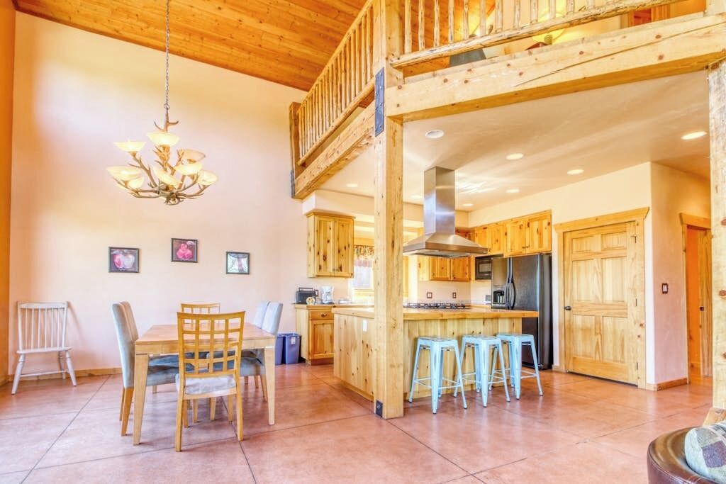 A spacious kitchen with wooden cabinets, a central island with stools, and a hanging chandelier.