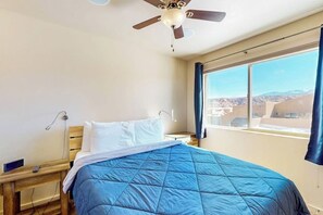 Ein Schlafzimmer mit Bett, Deckenventilator, Fenster mit Vorhängen und Blick ins Freie.