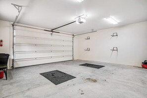 A clean, empty garage with a white garage door, two black mats on the floor, and ceiling lights. - Lovely Condo With Cozy Fireplace & Mountain Views - Great Location (Moab)