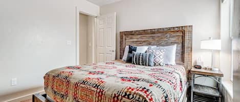A bedroom with a bed, a nightstand, a lamp, and a door.