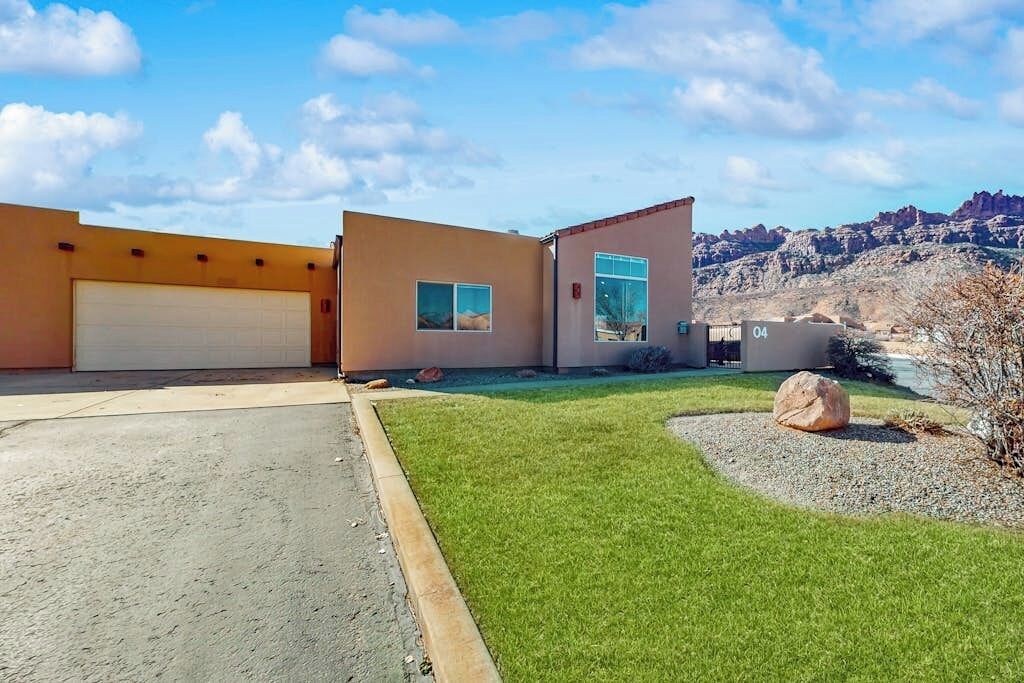 Ein modernes, zweistöckiges Haus mit Garage, gepflegtem Rasen und einer großen Felsformation.