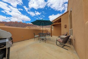 An outdoor patio with a table and chairs, a grill, and a view of a desert landscape. - Lovely 3BR Mountainview with Pool and Hot Tub (Moab)
