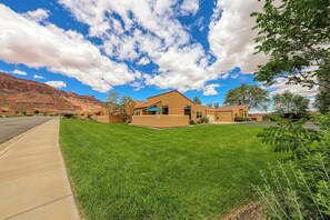 A residential property with a well-maintained lawn, a clear sky, and a mountain backdrop. - Lovely 3BR Mountainview with Pool and Hot Tub (Moab)