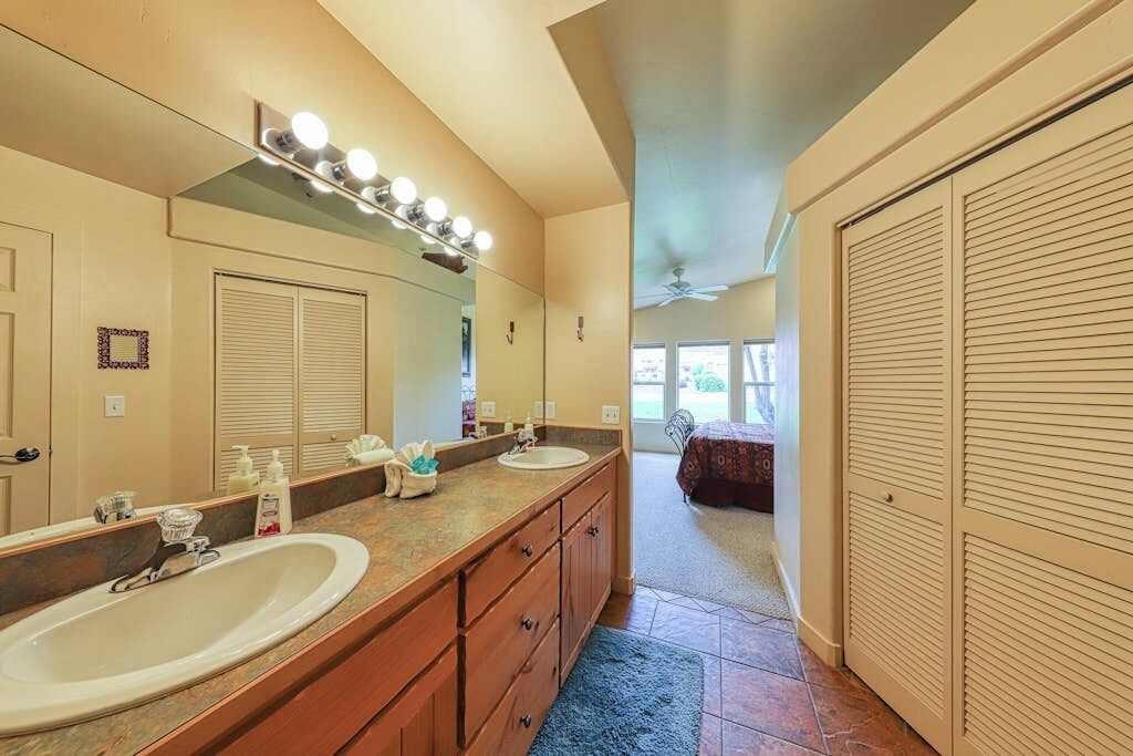 A bathroom with two sinks, a large mirror, vanity lights, and a ceiling fan.