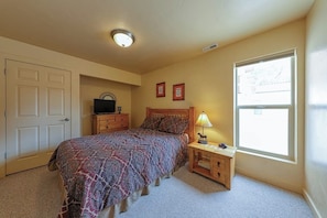 A bedroom with a bed, a nightstand, a lamp, a dresser, a television, and a window. - Lovely 3BR Mountainview with Pool and Hot Tub (Moab)